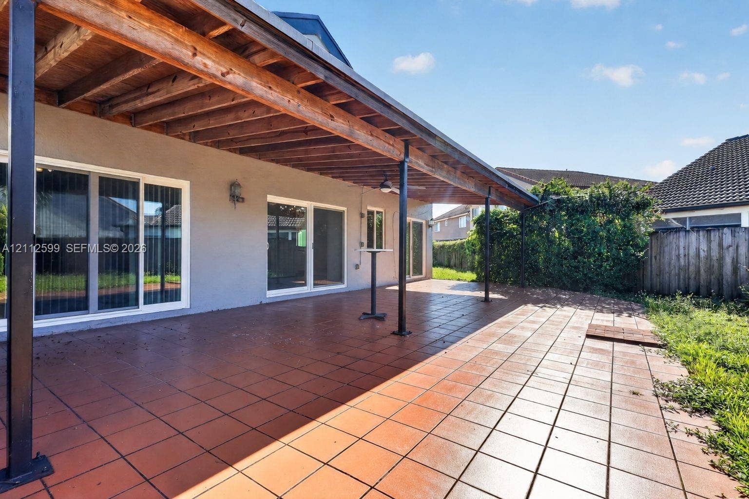 7974 NW 190th Terrace, Hialeah, FL 33015 Covered patio featuring ceramic tile flooring, exposed wood ceiling beams, metal support columns, and multiple sliding glass doors