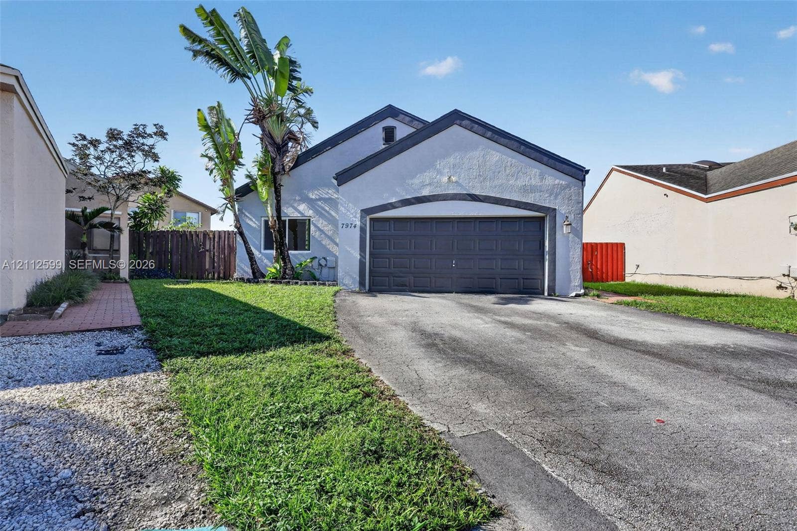 7974 NW 190th Terrace, Hialeah, FL 33015 Stucco exterior featuring a dual-gabled roofline, an attached two-car garage, and a paved driveway