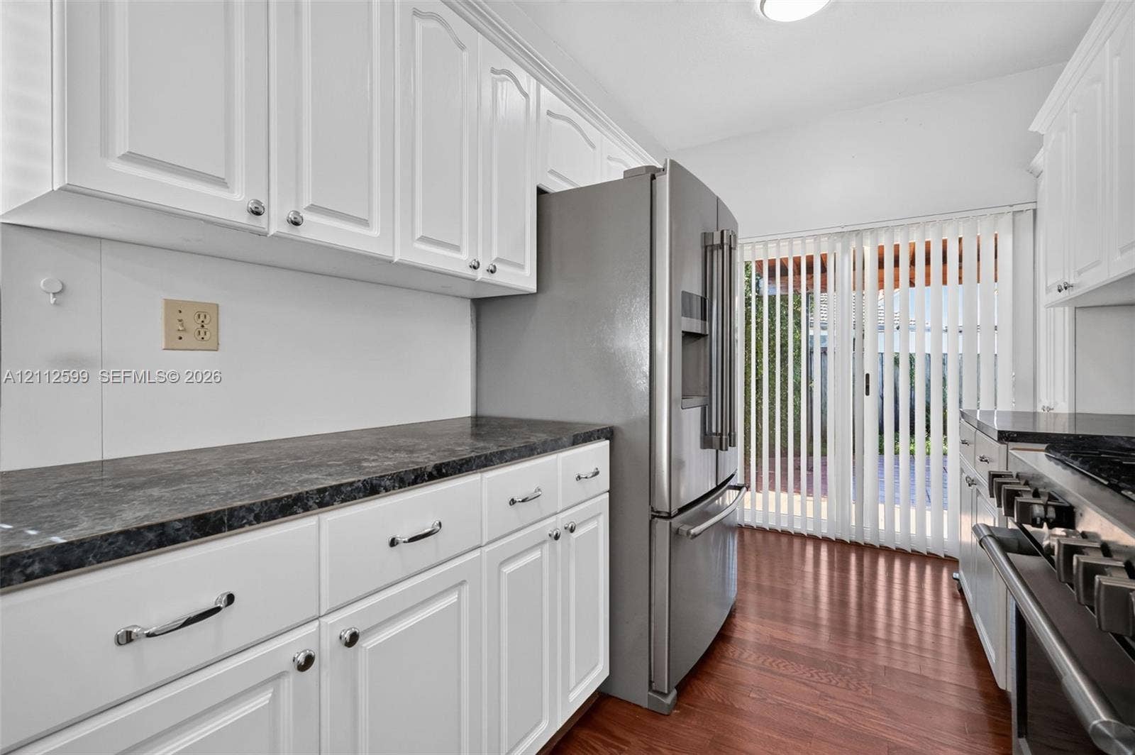 7974 NW 190th Terrace, Hialeah, FL 33015 Kitchen featuring white cabinetry, dark countertops, wood-finish flooring, stainless steel refrigerator, and sliding glass doors