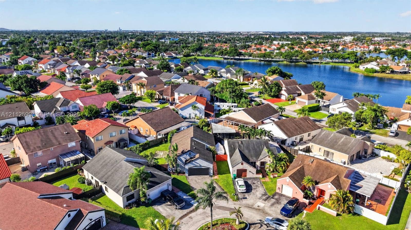 7974 NW 190th Terrace, Hialeah, FL 33015 Aerial perspective of a residential neighborhood featuring multi-pitch roofs, paved driveways, manicured lawns, and proximity to a large community lake