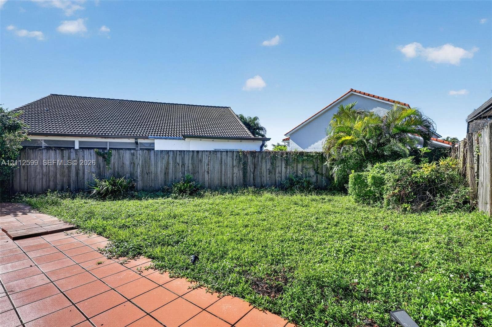 7974 NW 190th Terrace, Hialeah, FL 33015 Rear exterior featuring a fenced perimeter, expansive lawn, and terracotta-style tiled patio