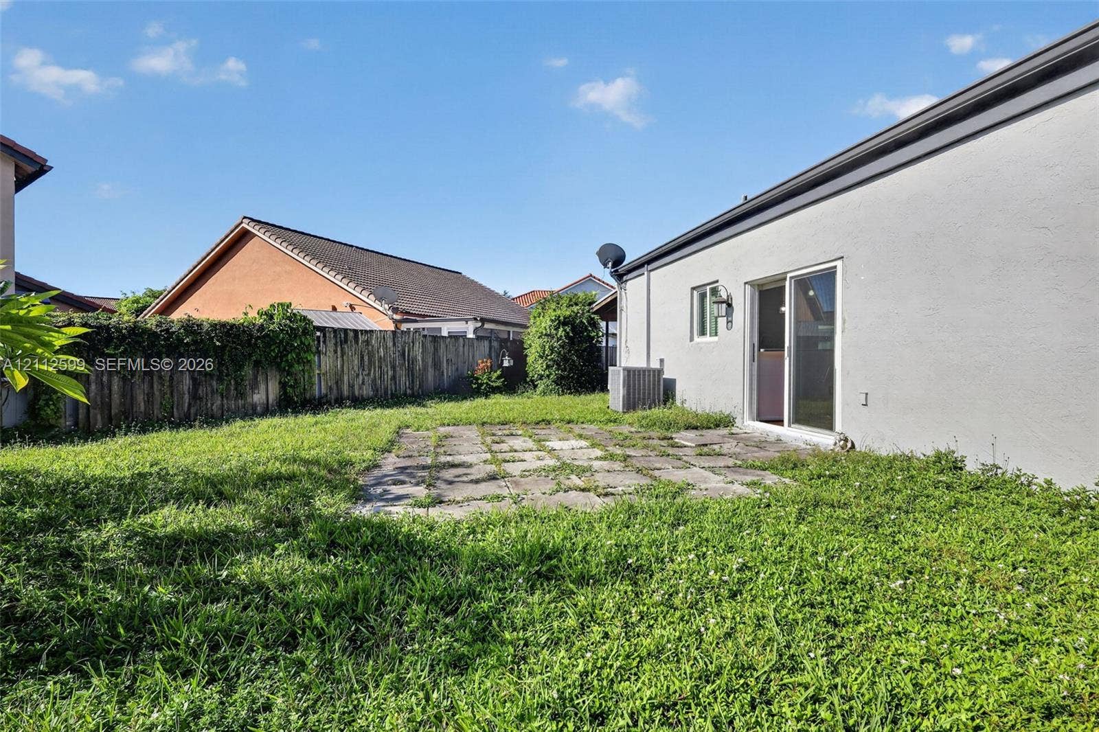 7974 NW 190th Terrace, Hialeah, FL 33015 Rear exterior featuring a concrete patio, stucco siding, sliding glass door, and a wooden privacy fence