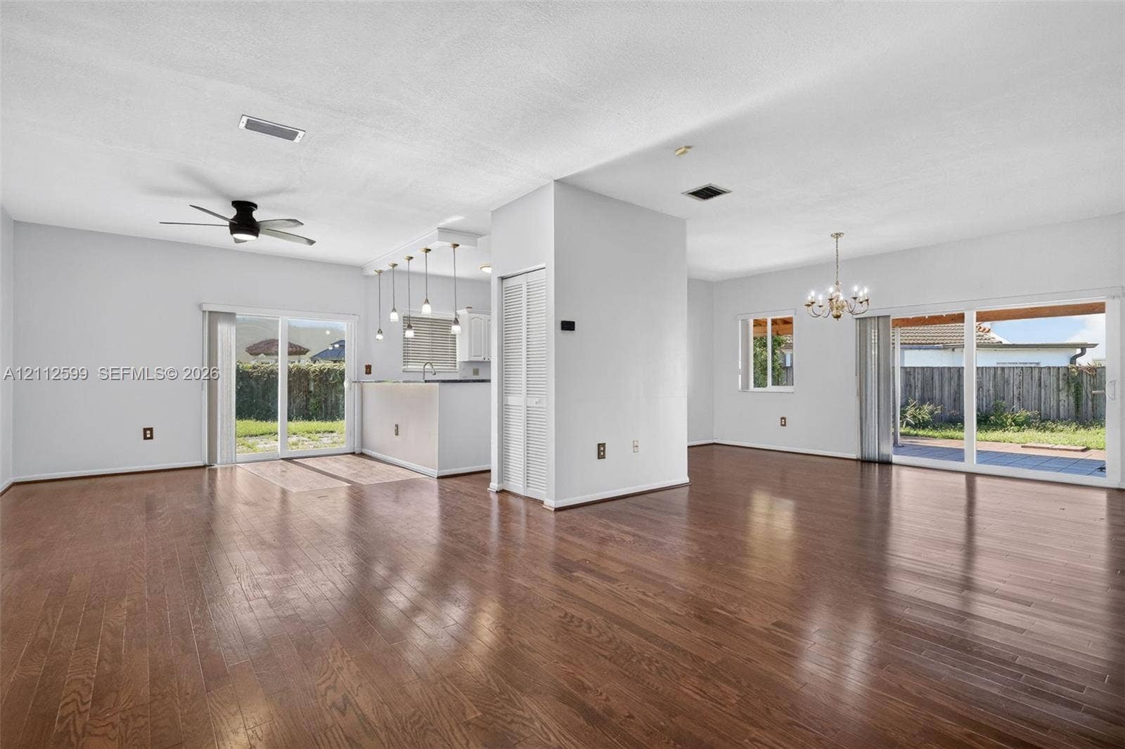 7974 NW 190th Terrace, Hialeah, FL 33015 Open interior space featuring wood-finish flooring, two sets of glass sliding doors, a central ceiling fan, and pendant lighting over a built-in counter