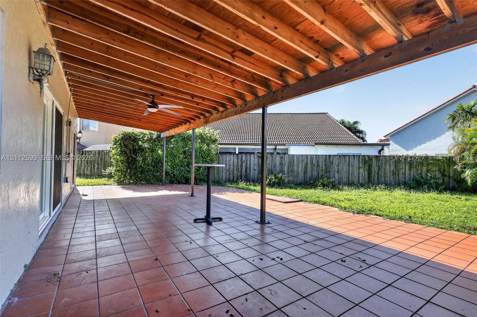 7974 NW 190th Terrace, Hialeah, FL 33015 Covered rear patio featuring a wood-beam pergola, tiled flooring, integrated ceiling fan, and exterior wall-mounted lighting