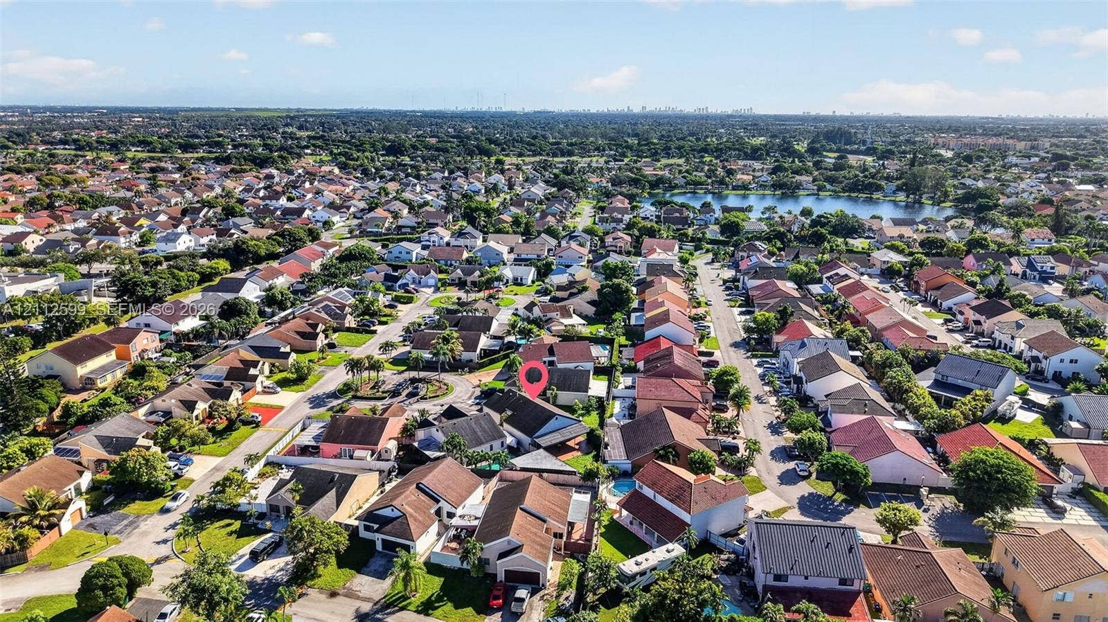 7974 NW 190th Terrace, Hialeah, FL 33015 Aerial perspective of a suburban neighborhood featuring a grid-pattern street layout, dense residential housing, and a central lake