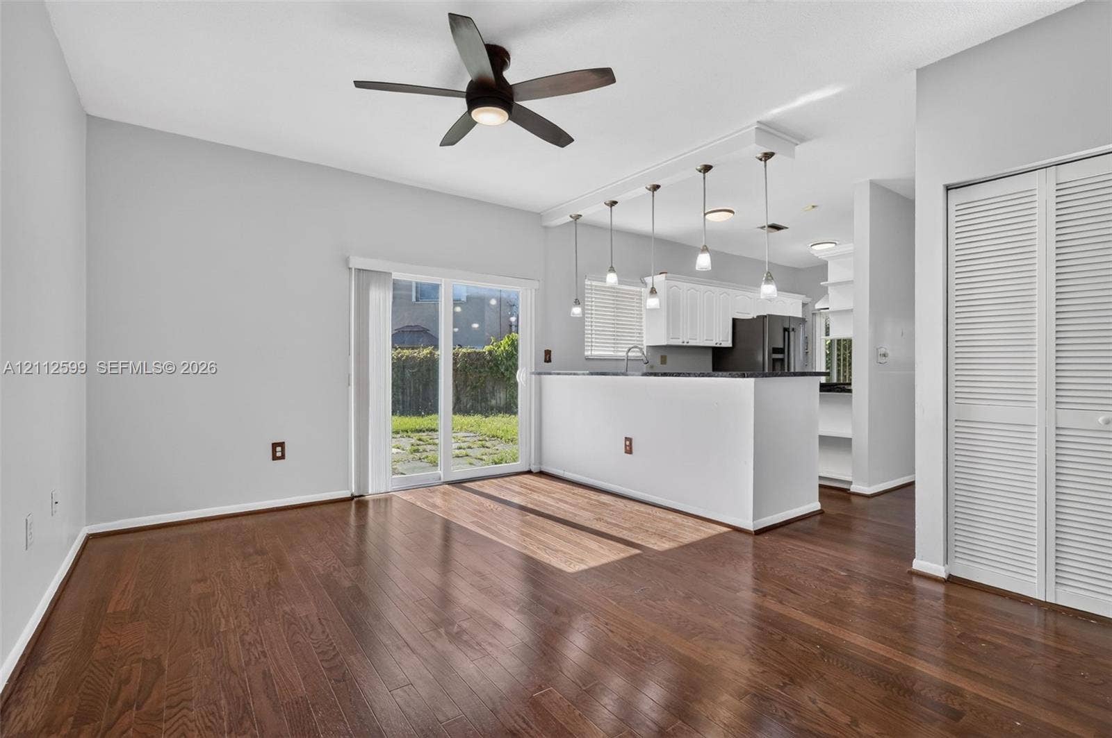 7974 NW 190th Terrace, Hialeah, FL 33015 Wood-finish flooring, kitchen peninsula with pendant lighting, sliding glass door, white louvered closet doors, and ceiling fan with integrated light