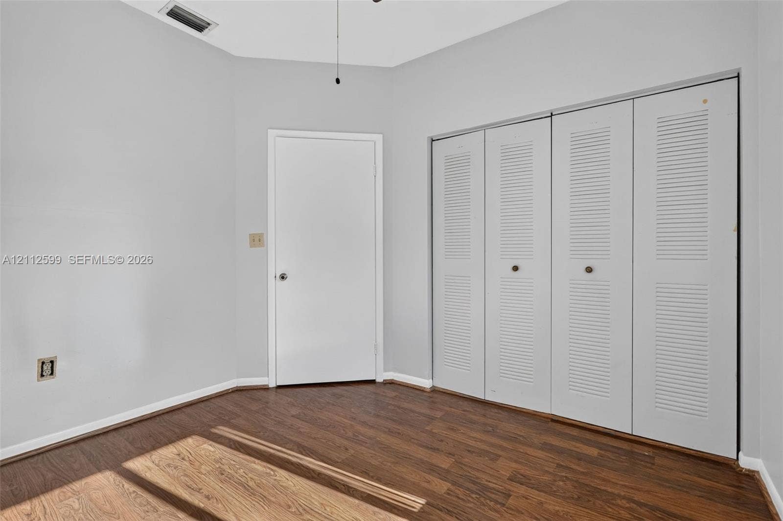7974 NW 190th Terrace, Hialeah, FL 33015 Interior room featuring wood-finish flooring, neutral wall paint, and floor-to-ceiling closet cabinetry with white louvered bifold doors