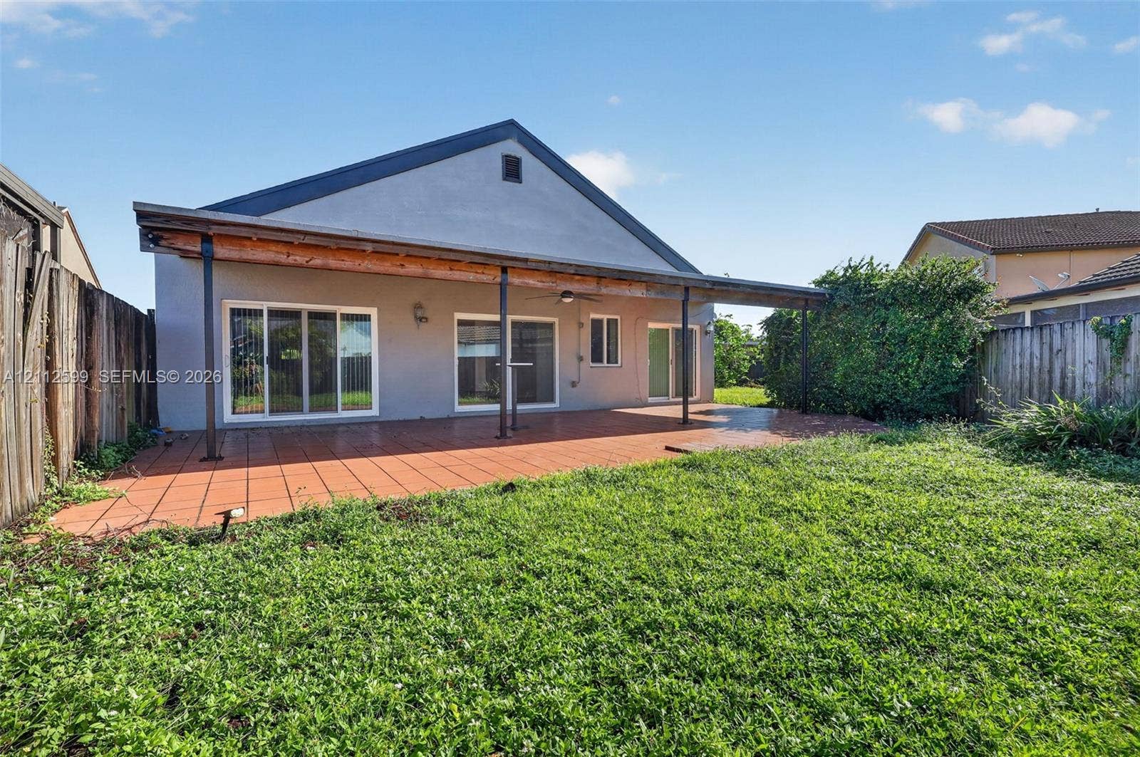 7974 NW 190th Terrace, Hialeah, FL 33015 Rear exterior featuring a covered patio with tile flooring, three sliding glass doors, and a wood-beam support structure