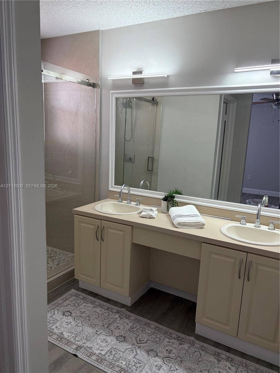 Dual-sink vanity with solid-surface countertop, full-width mirror, inset cabinetry, and glass-enclosed shower