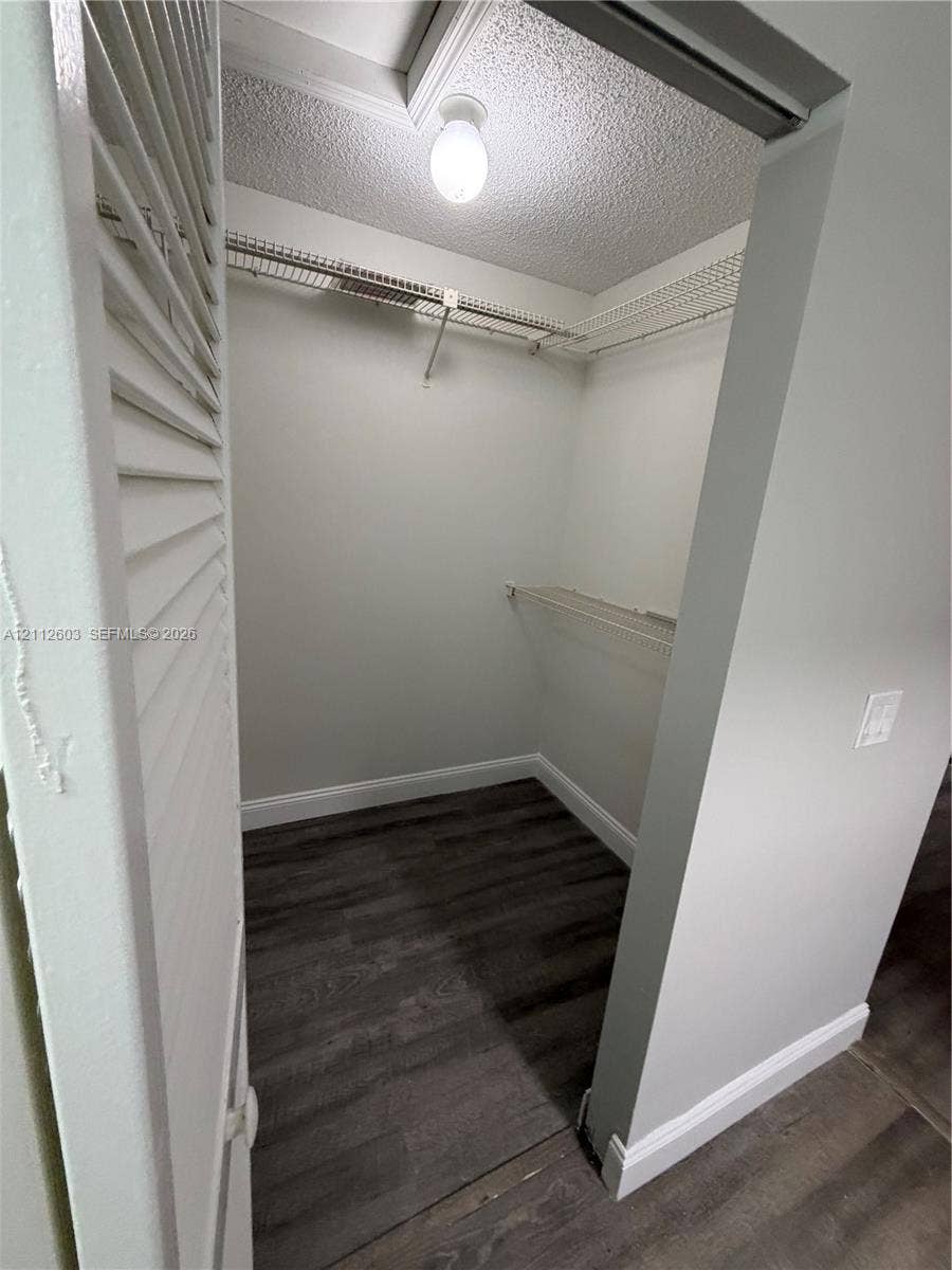 Walk-in closet featuring wood-finish flooring, white louvered door, and built-in wire shelving