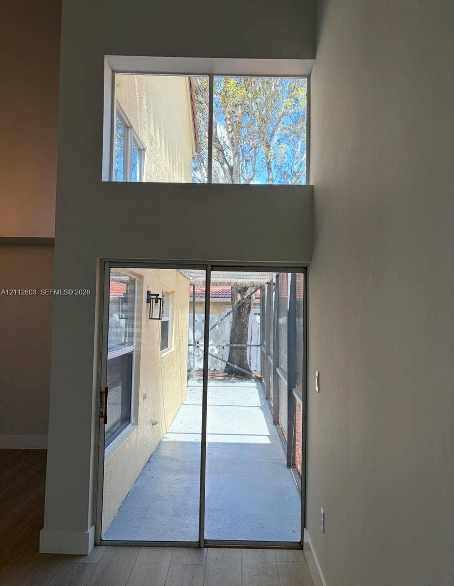 Double-height wall featuring a sliding glass door and an upper transom window, wood-finish flooring, and a screened-in patio area