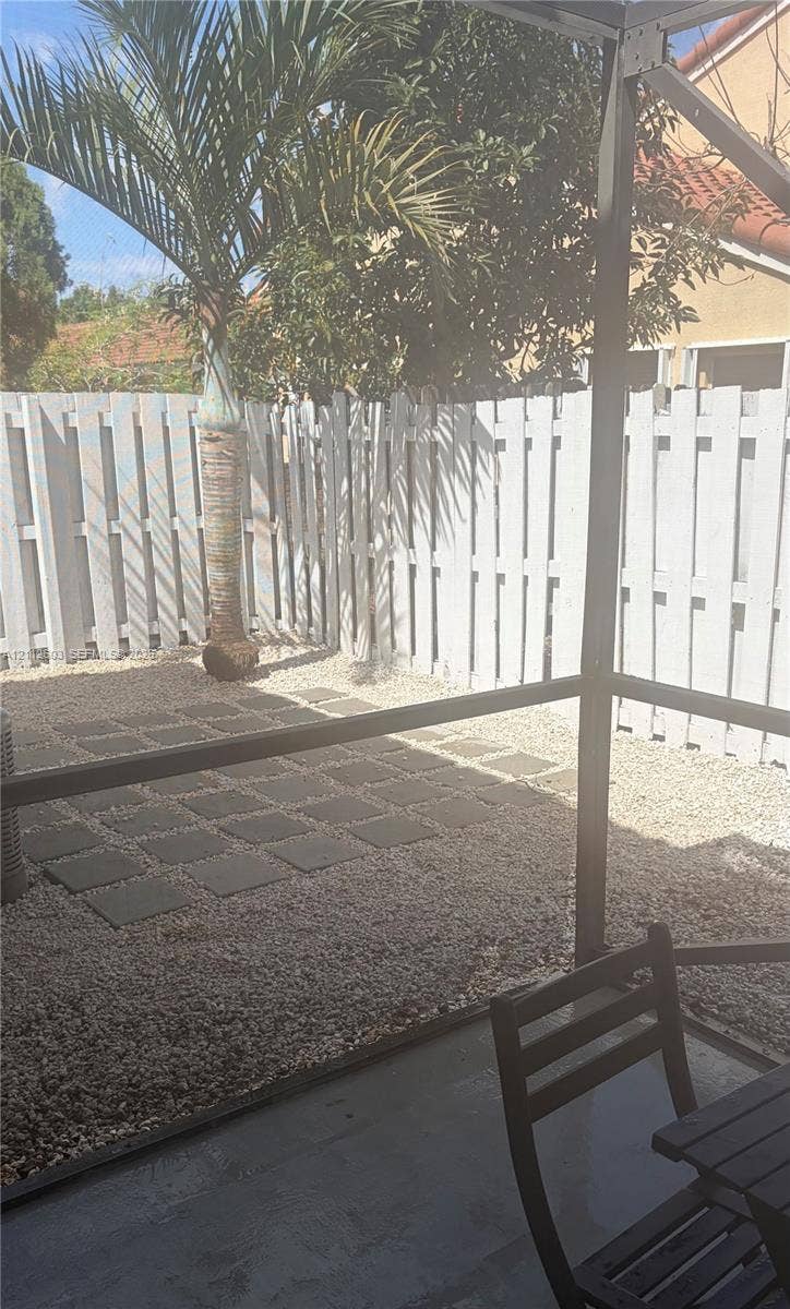 Enclosed patio with metal framing, featuring a gravel-surfaced outdoor area, concrete paver accents, and a vertical privacy fence