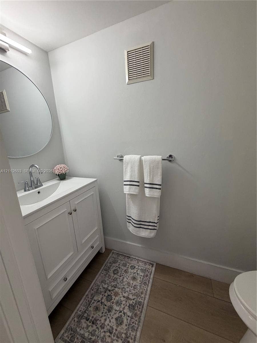 Guest Bathroom. Brand new white cabinetry vanity with a polished chrome faucet, round wall mirror, and wood-finish flooring