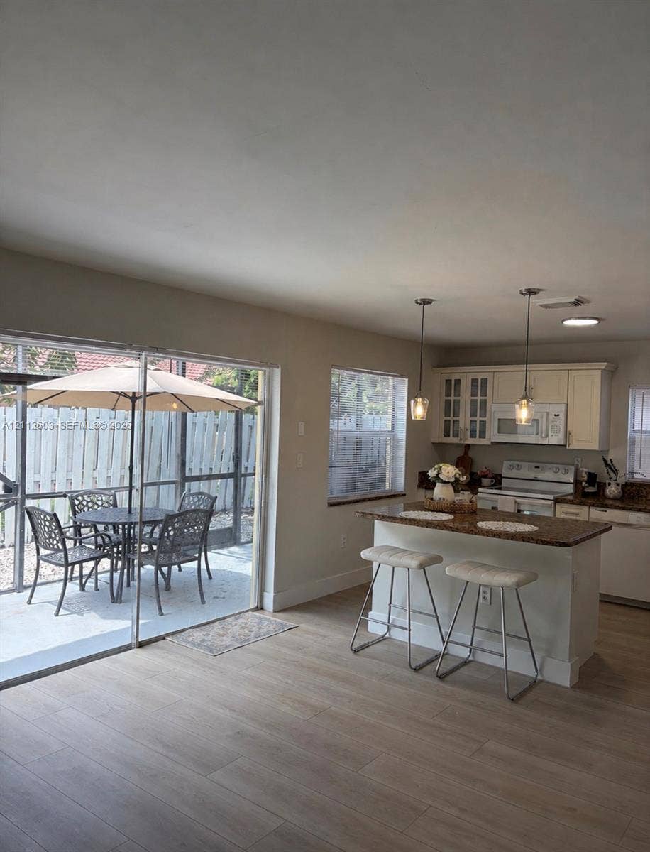 Kitchen featuring white cabinetry, granite countertops, a breakfast bar, dual pendant lighting, and wood-finish flooring with glass sliding doors to a screened-in patio
