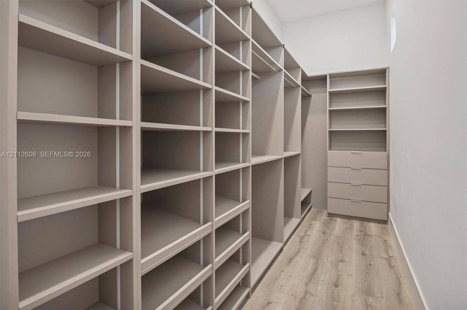 Custom floor-to-ceiling cabinetry, integrated shelving units, dedicated hanging rods, built-in soft-close drawers, and wood-finish flooring