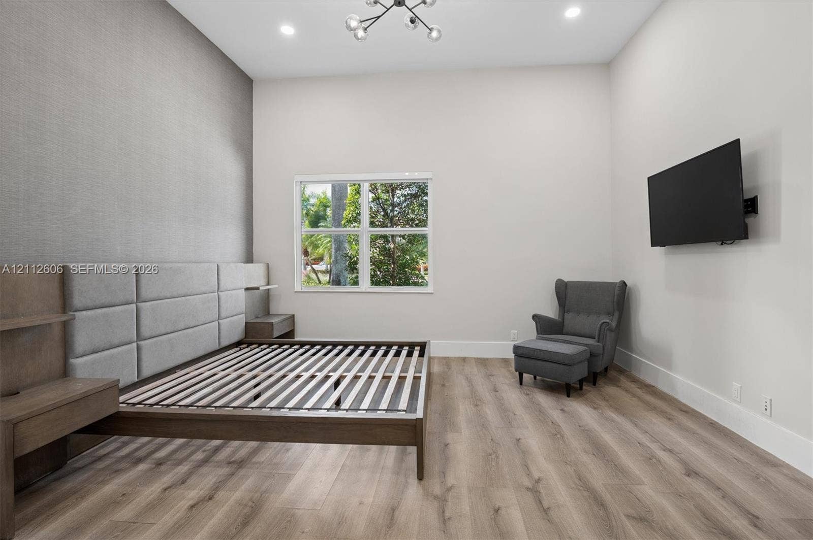 High-ceilinged room featuring wood-finish flooring, a neutral color palette, integrated wall-mounted lighting fixture, and a textured accent wall