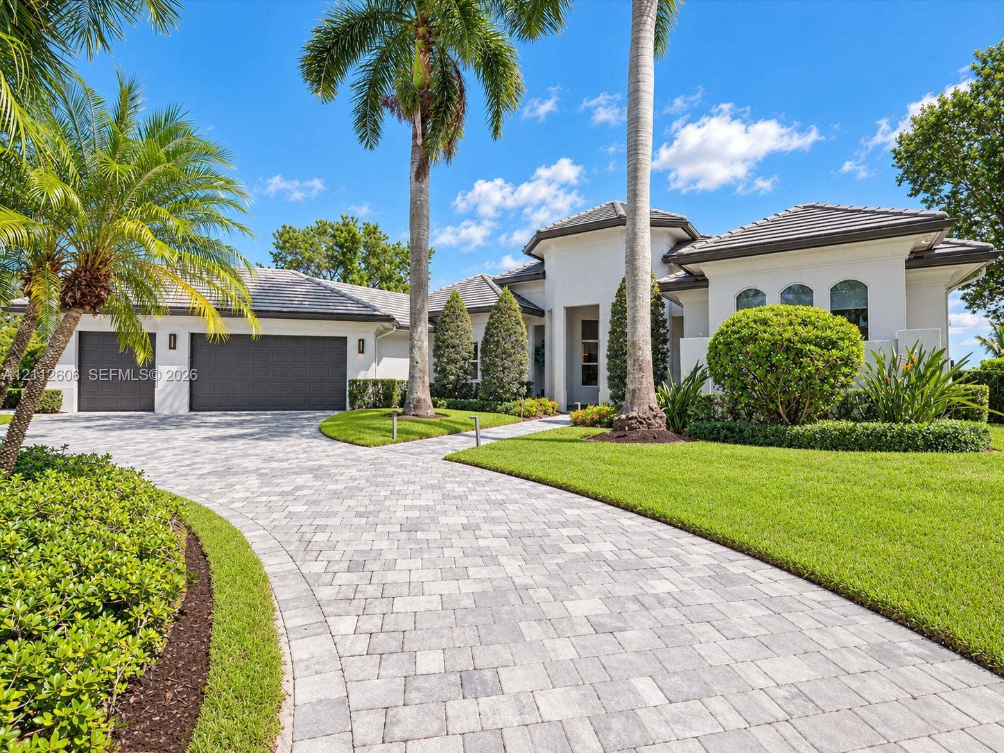 Stucco exterior featuring a multi-car garage, concrete tile roof, paver driveway, and professional landscaping