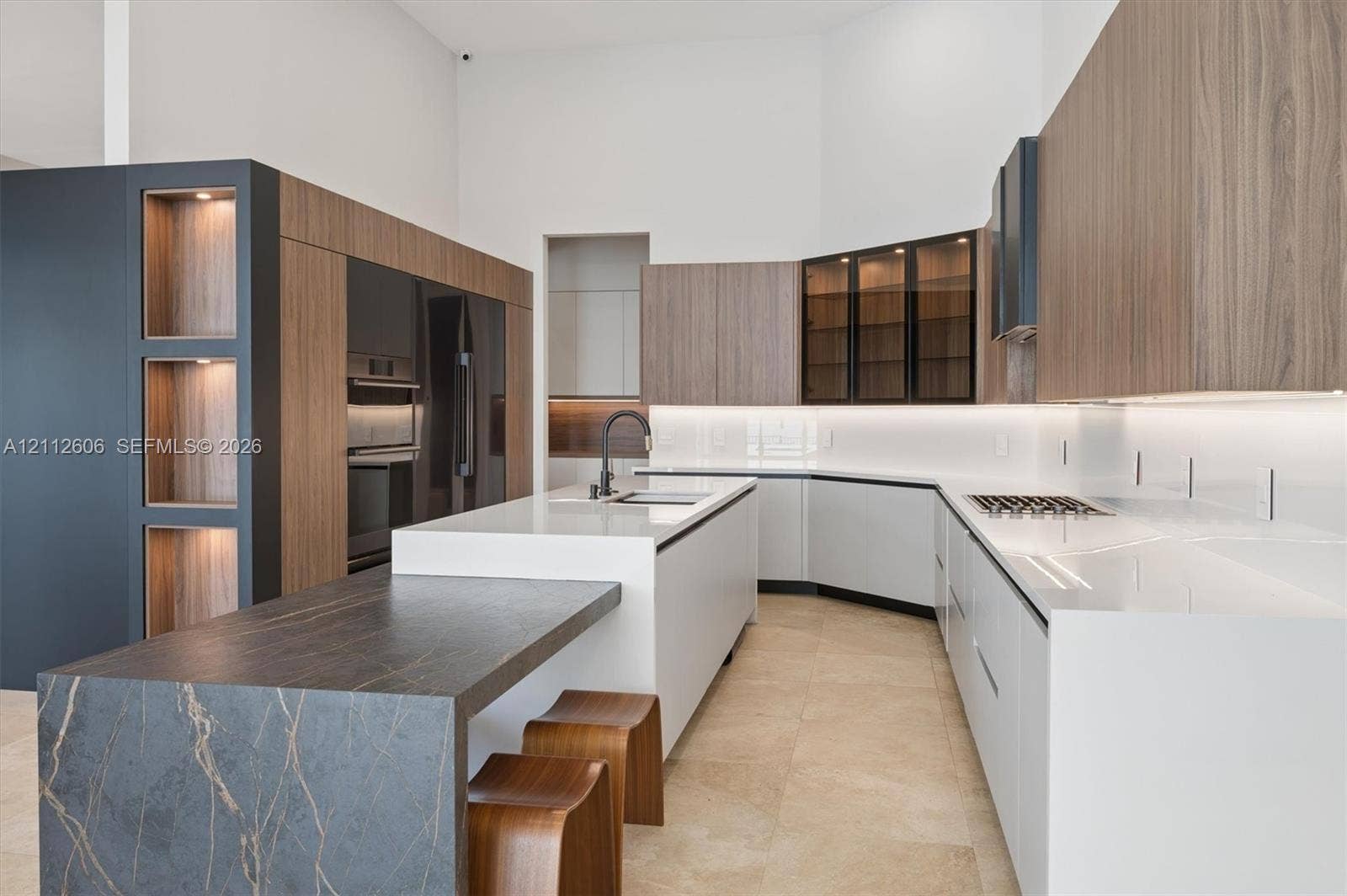 Kitchen featuring white solid-surface countertops, wood-finish cabinetry, a large stone-topped kitchen island, built-in wall ovens, and under-cabinet integrated lighting