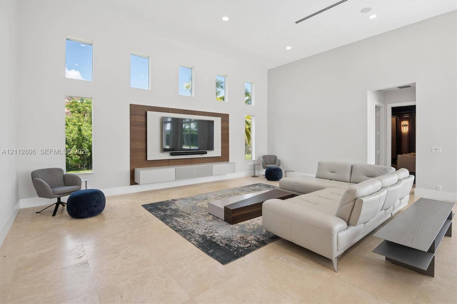 High-ceilinged living area featuring stone flooring, integrated wood-paneled media wall, wall-mounted floating cabinetry, and floor-to-ceiling vertical windows
