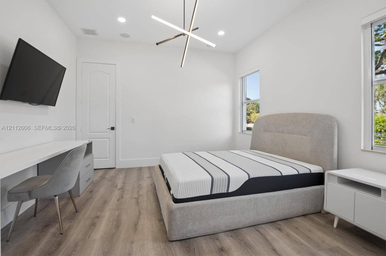 Wood-finish flooring, geometric architectural ceiling light fixture, recessed lighting, and white walls featuring dual windows