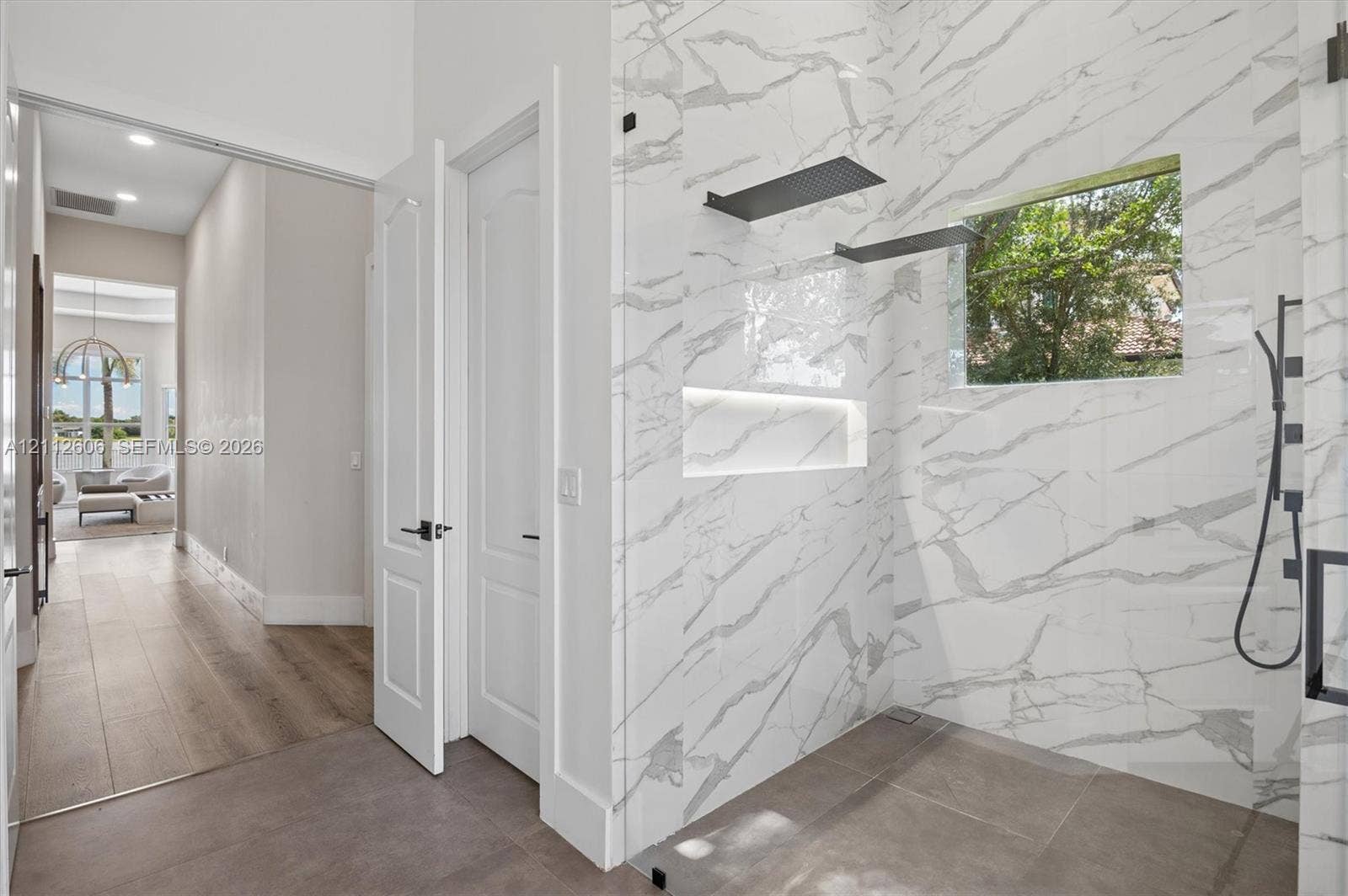 Walk-in shower featuring floor-to-ceiling stone-patterned tile, a recessed niche, black matte hardware, and an integrated glass enclosure, complemented by large-format tile flooring