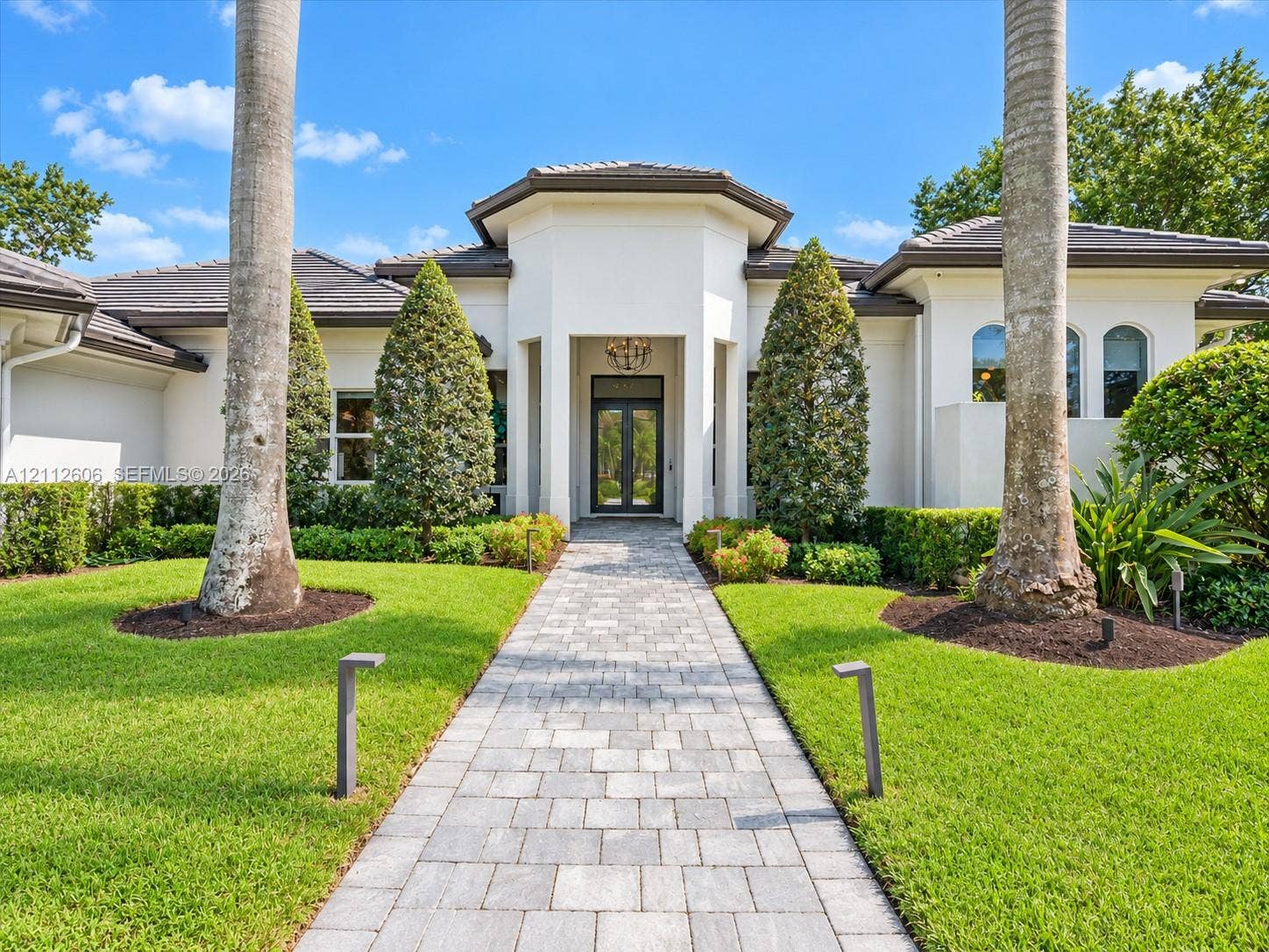 Stucco exterior featuring a hipped tile roof, an arched entryway, stone-paver walkway, and manicured landscaping