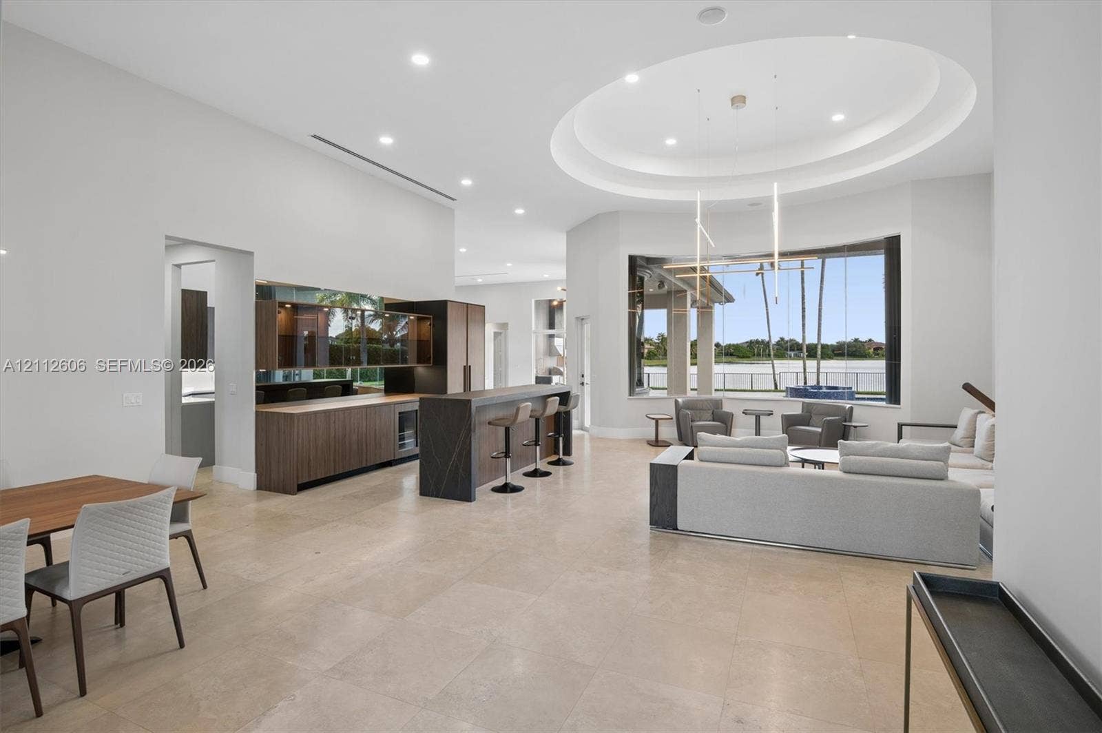 Open-concept interior featuring large-format tile flooring, a built-in wet bar with wood-finish cabinetry, an oval tray ceiling, recessed lighting, and expansive windows