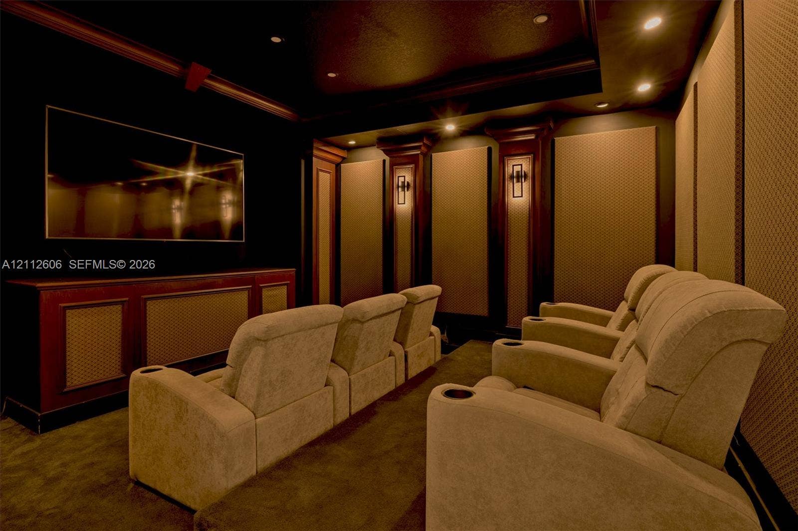 Dedicated media room featuring recessed ceiling lighting, wall-mounted acoustic paneling, integrated wood cabinetry, and wall sconces