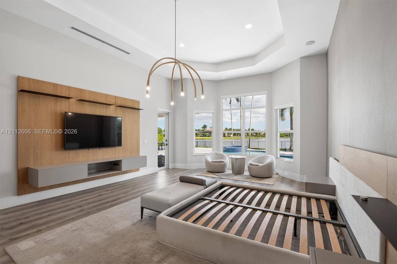 Tray ceiling with recessed lighting, wood-finish flooring, custom wood-paneled media wall with integrated shelving, and large windows