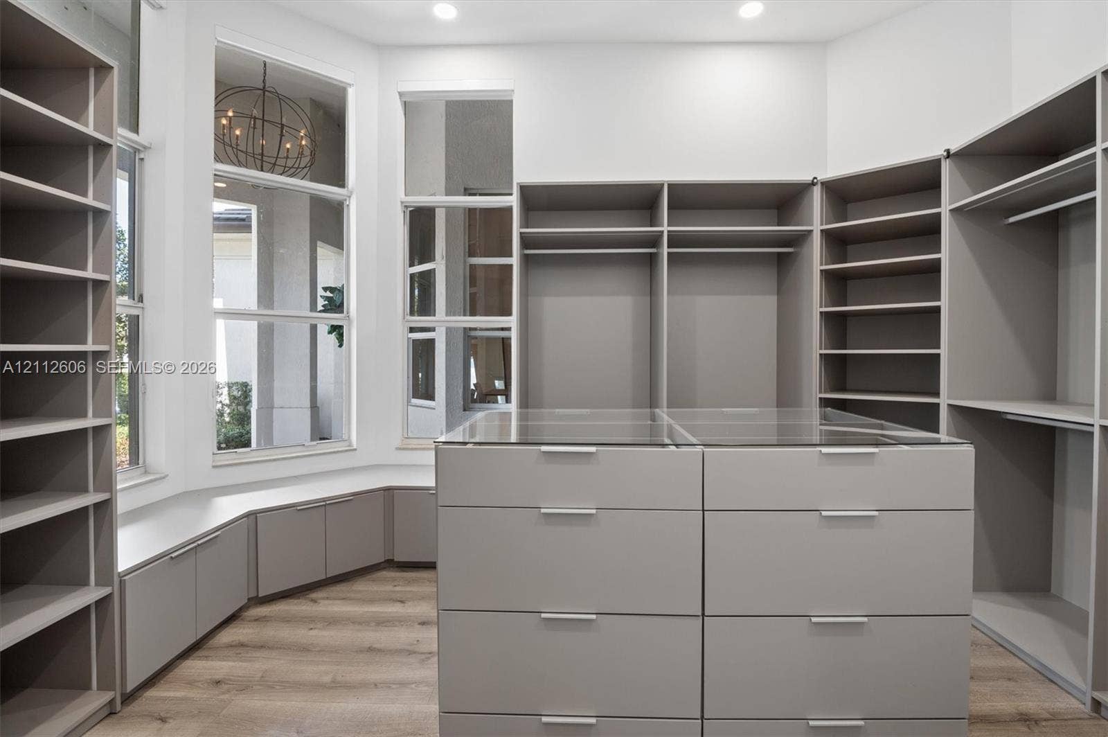 Custom built-in storage system featuring floor-to-ceiling shelving, hanging rods, and a central island with glass-top drawers
