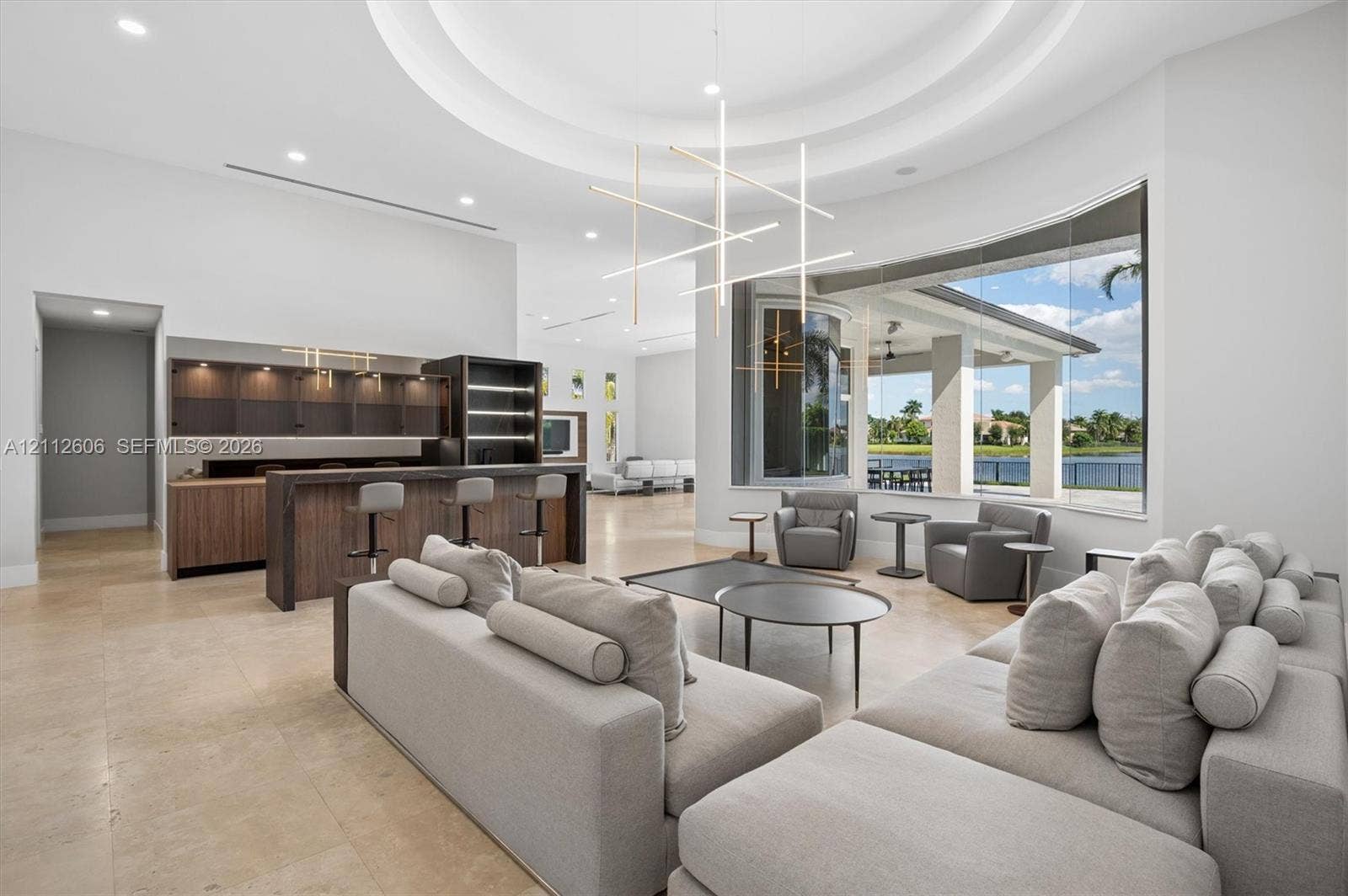Open-concept space featuring a circular tray ceiling, large-format tile flooring, built-in wet bar with wood-finish cabinetry, contemporary linear chandelier, and expansive floor-to-ceiling windows