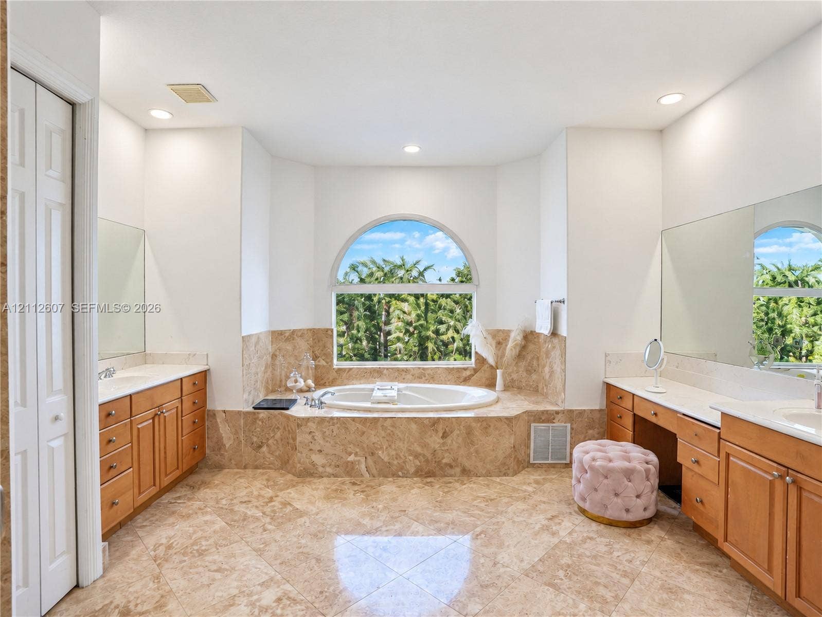 14443 S Jockey Circle S, Davie, FL 33330 Bathroom featuring dual wooden vanities, stone-tile flooring, jetted soaking tub with arched window surround, and large wall-mounted mirrors