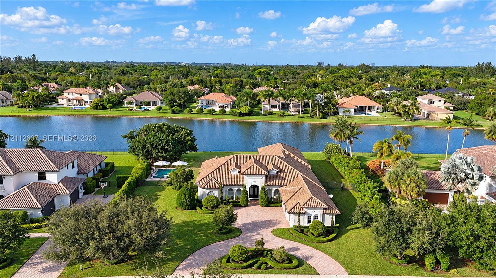 14443 S Jockey Circle S, Davie, FL 33330 Waterfront residence featuring a tile roof, paved circular driveway, manicured landscaping, and a private swimming pool