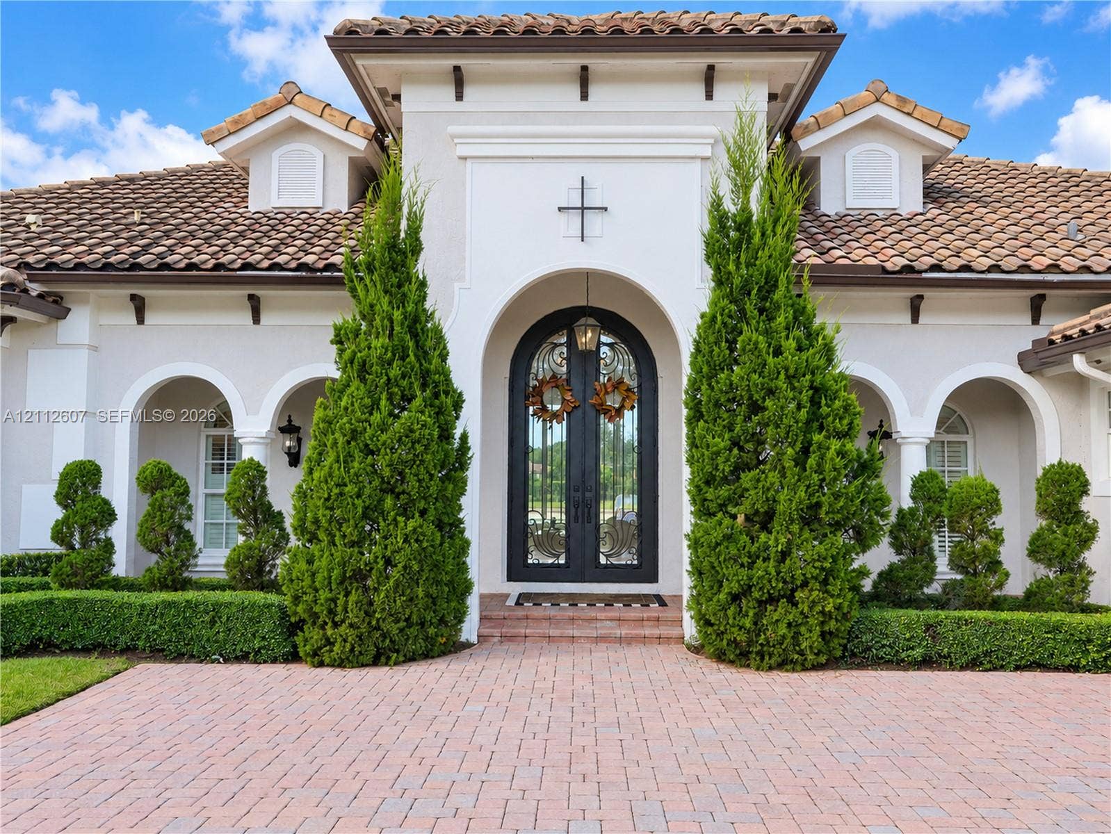 14443 S Jockey Circle S, Davie, FL 33330 Stucco exterior featuring an arched entryway, double iron-detail glass doors, clay tile roof, and brick paver driveway