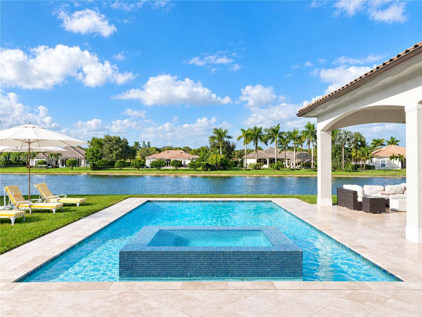 14443 S Jockey Circle S, Davie, FL 33330 Rectangular swimming pool with an integrated tile-finished spa, expansive stone-paver deck, covered lanai, and waterfront positioning