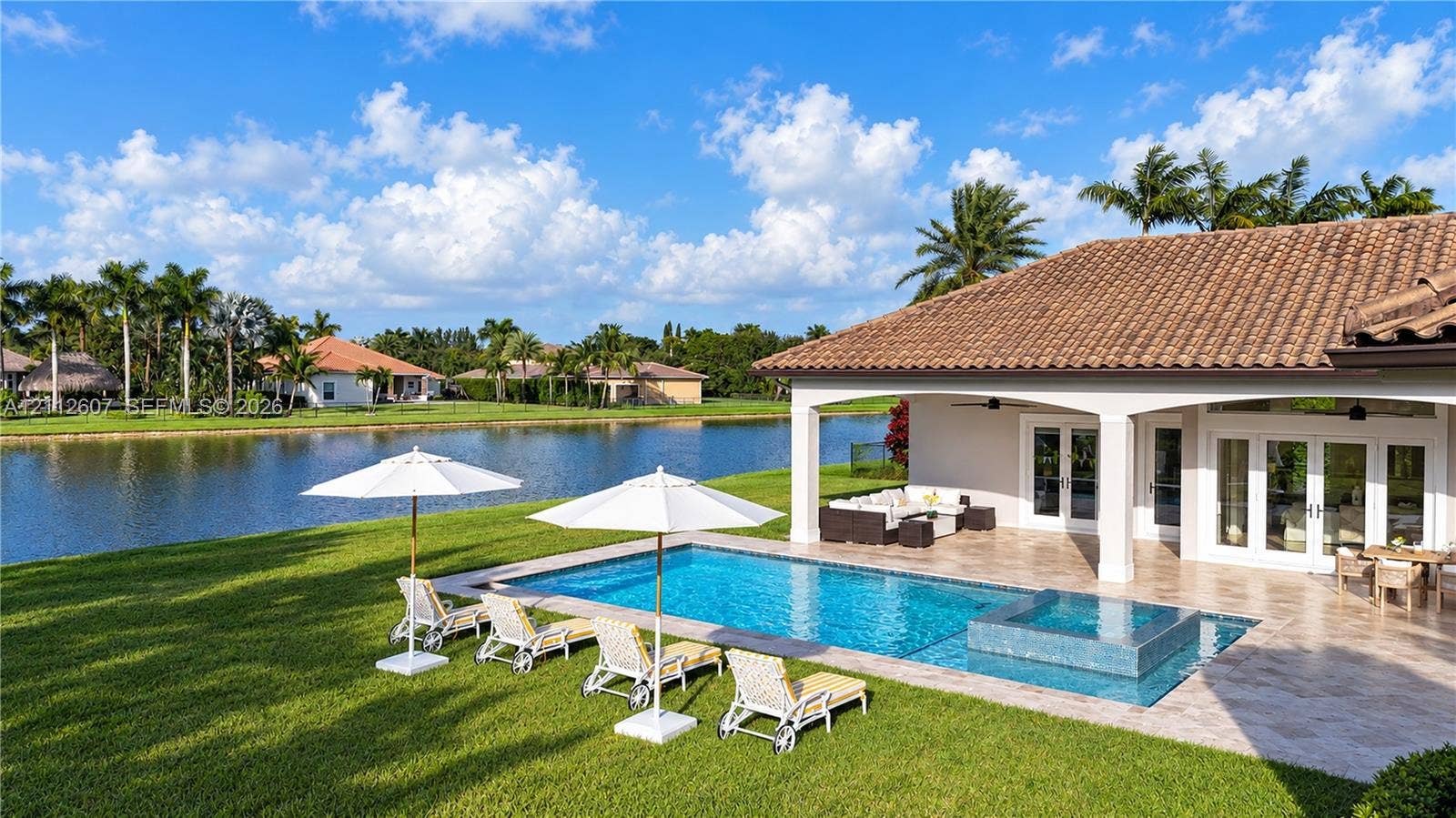 14443 S Jockey Circle S, Davie, FL 33330 Rear exterior featuring a covered patio, a rectangular swimming pool with an integrated spa, stone-tile decking, and a waterfront location