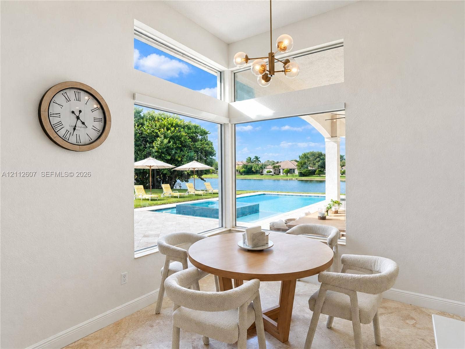 14443 S Jockey Circle S, Davie, FL 33330 High-ceiling dining area featuring expansive corner windows, a multi-globe metal chandelier, and stone-finish flooring with outdoor water and pool access