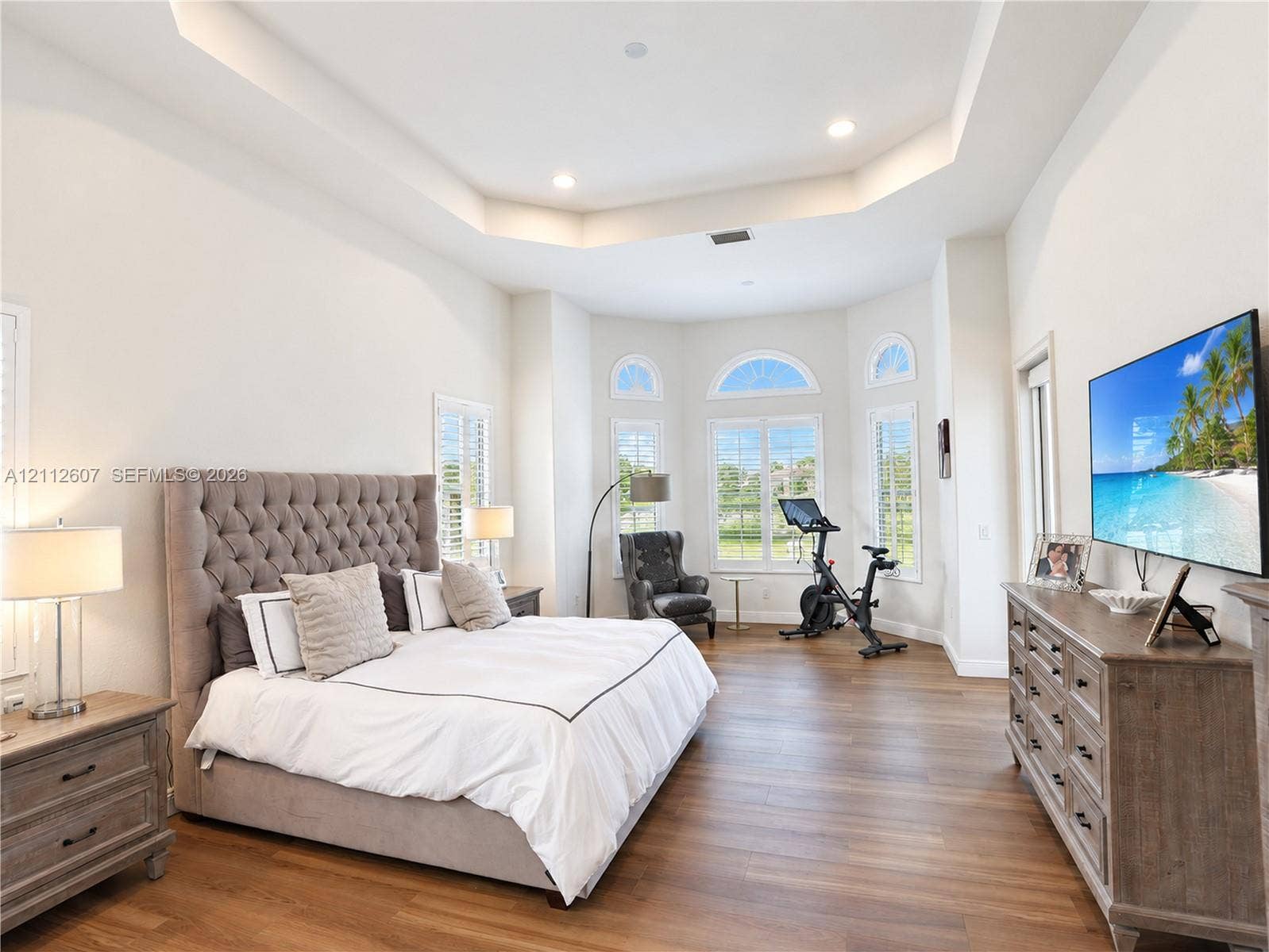 14443 S Jockey Circle S, Davie, FL 33330 Tray ceiling with recessed lighting, wood-finish flooring, and expansive bay windows featuring arched transoms and plantation shutters