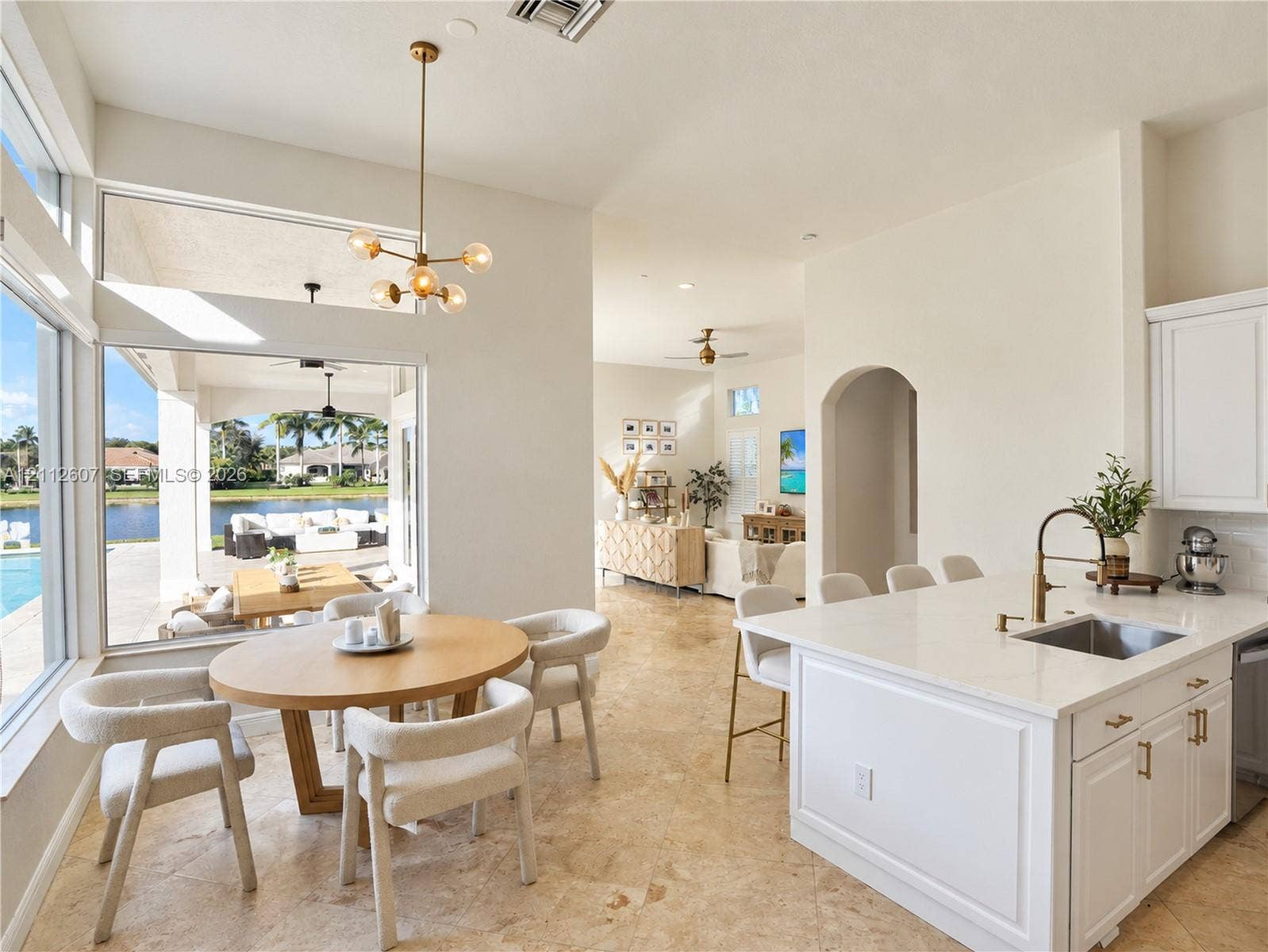 14443 S Jockey Circle S, Davie, FL 33330 Open-concept kitchen featuring an island with stone-surface countertop, undermount sink, and metallic faucet hardware, complemented by natural stone flooring and a multi-light pendant fixture