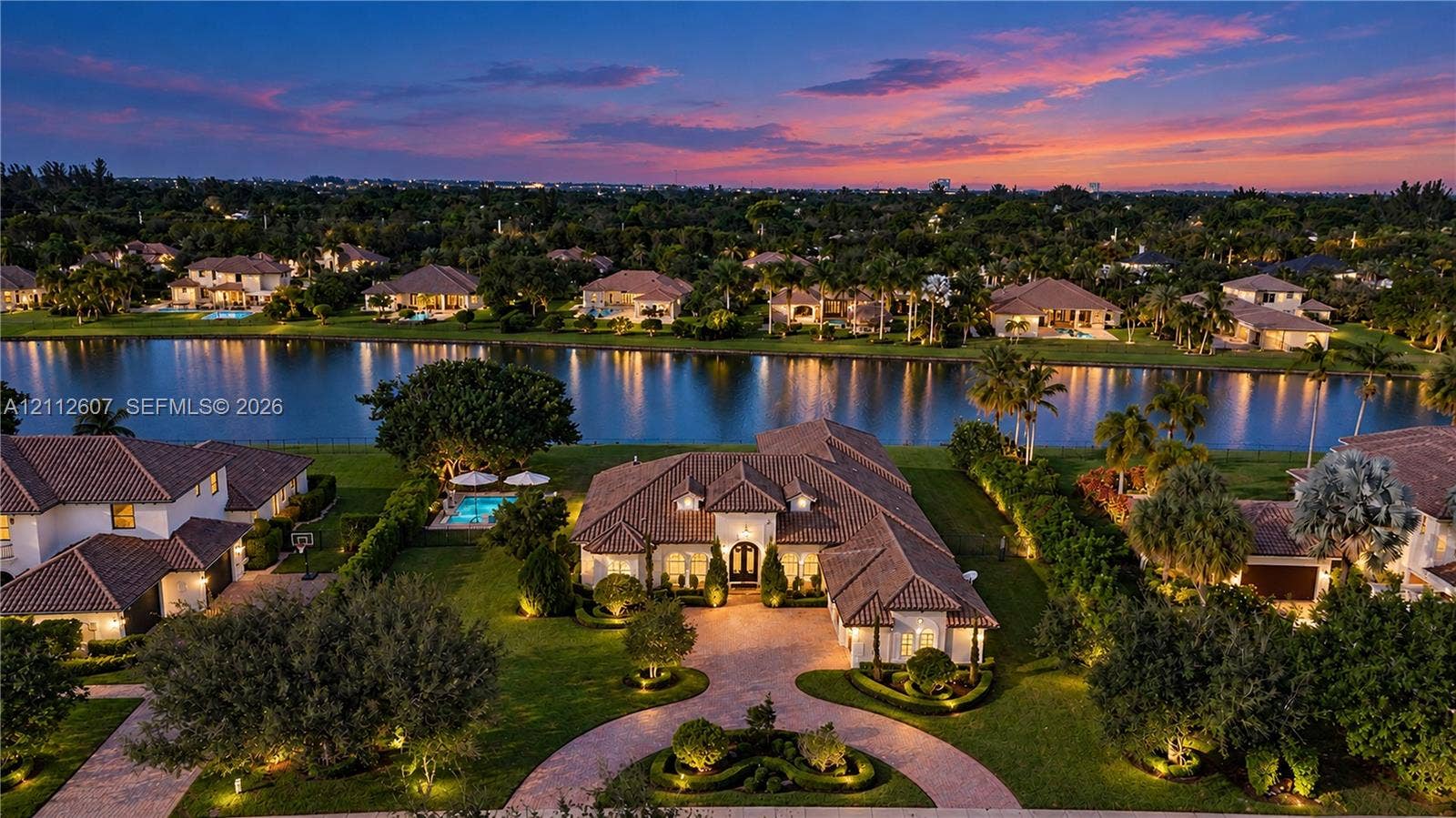 14443 S Jockey Circle S, Davie, FL 33330 Aerial perspective featuring a waterfront estate with a tile roof, paved circular driveway, manicured landscaping, and a pool