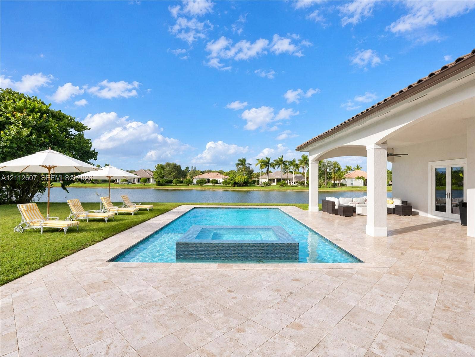 14443 S Jockey Circle S, Davie, FL 33330 Covered patio with natural stone flooring, swimming pool featuring an integrated spa, and lawn area with water frontage