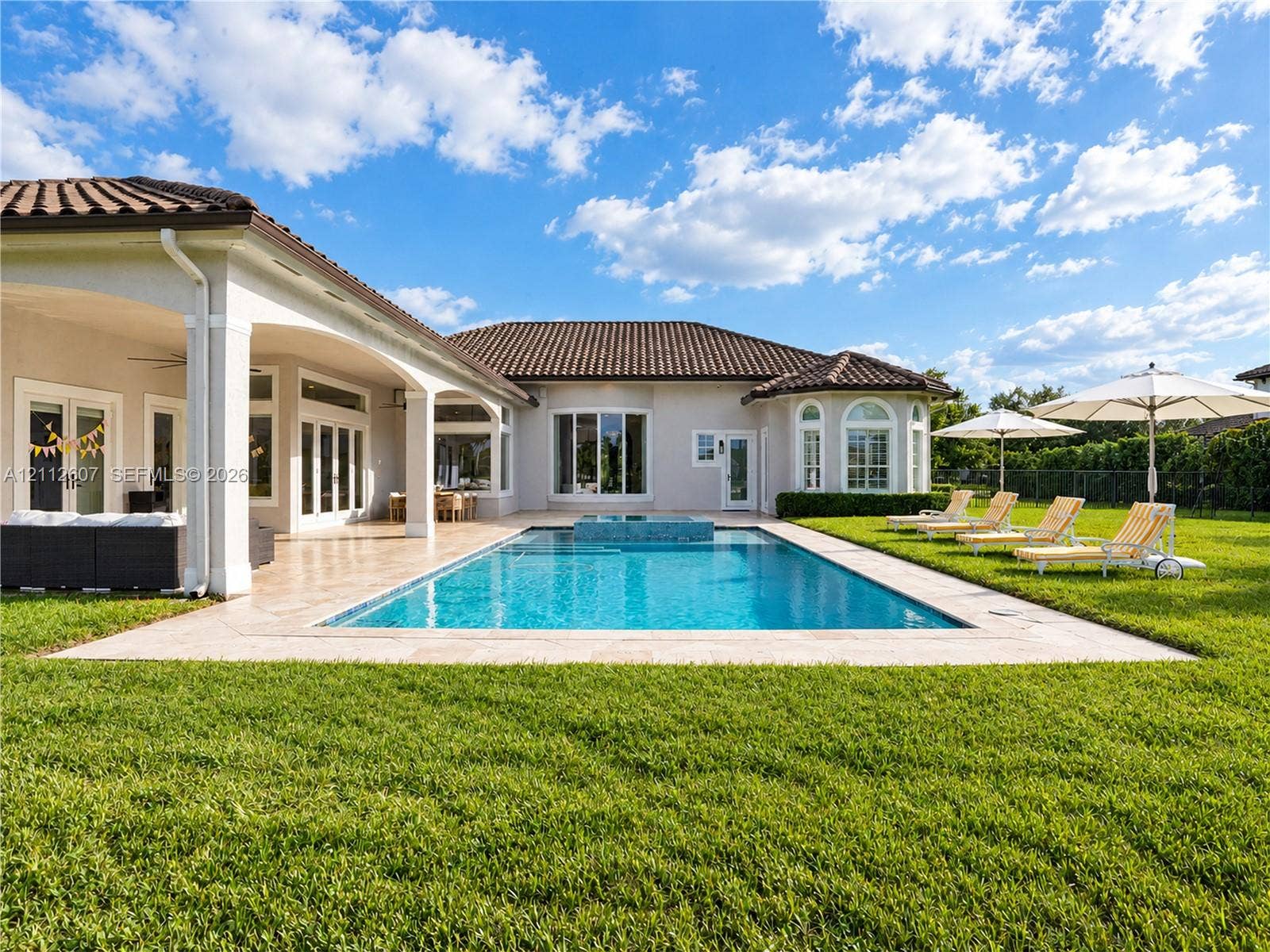14443 S Jockey Circle S, Davie, FL 33330 Stucco exterior with a tiled roof featuring a covered lanai, inground pool with an integrated spa, and expansive lawn