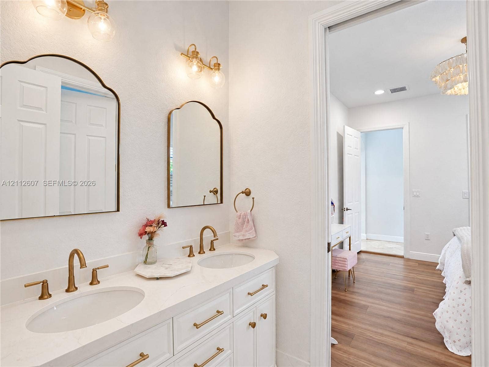 14443 S Jockey Circle S, Davie, FL 33330 Dual-sink vanity with a white solid-surface countertop, brass-toned fixtures, arched wall-mounted mirrors, and coordinated wall sconces
