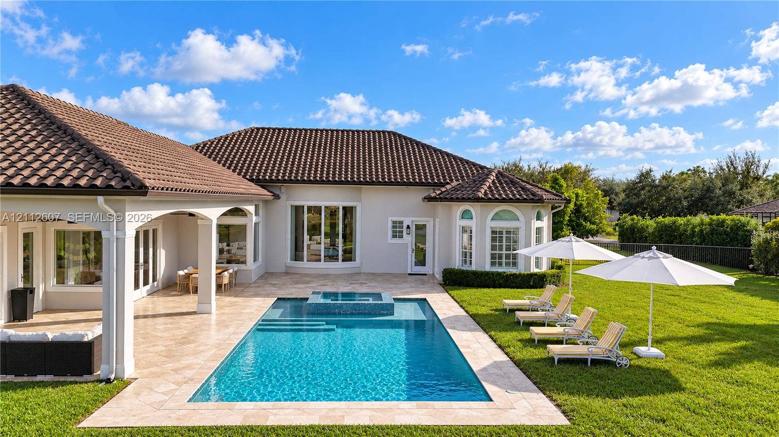 14443 S Jockey Circle S, Davie, FL 33330 Rear exterior featuring a covered patio, a rectangular swimming pool with an integrated spa, stone-paver decking, and a manicured lawn