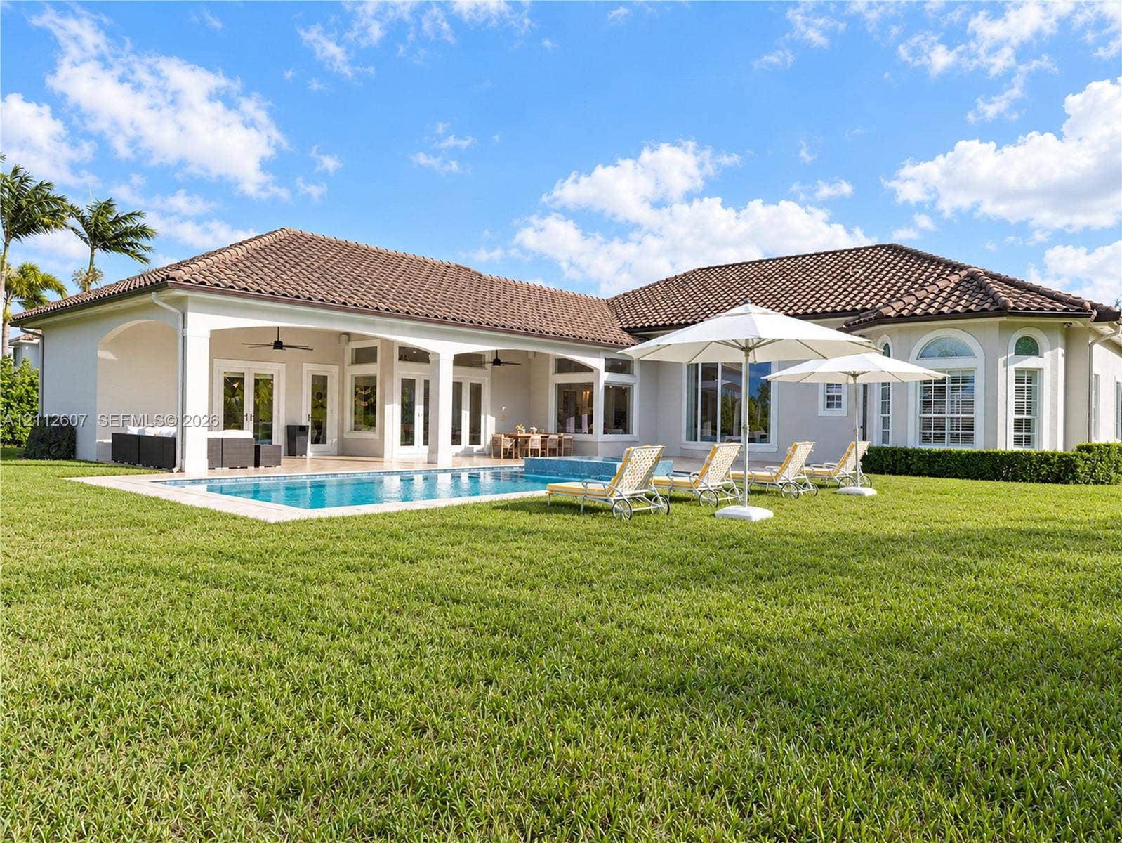 14443 S Jockey Circle S, Davie, FL 33330 Rear exterior featuring a tile roof, covered patio with recessed lighting, in-ground pool with integrated spa, and expansive lawn