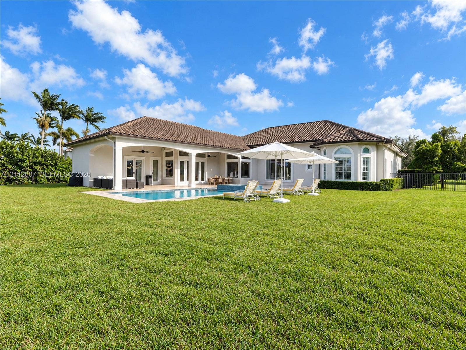 14443 S Jockey Circle S, Davie, FL 33330 Exterior featuring a tile roof, covered patio with arched supports, built-in swimming pool with masonry deck, and expansive lawn