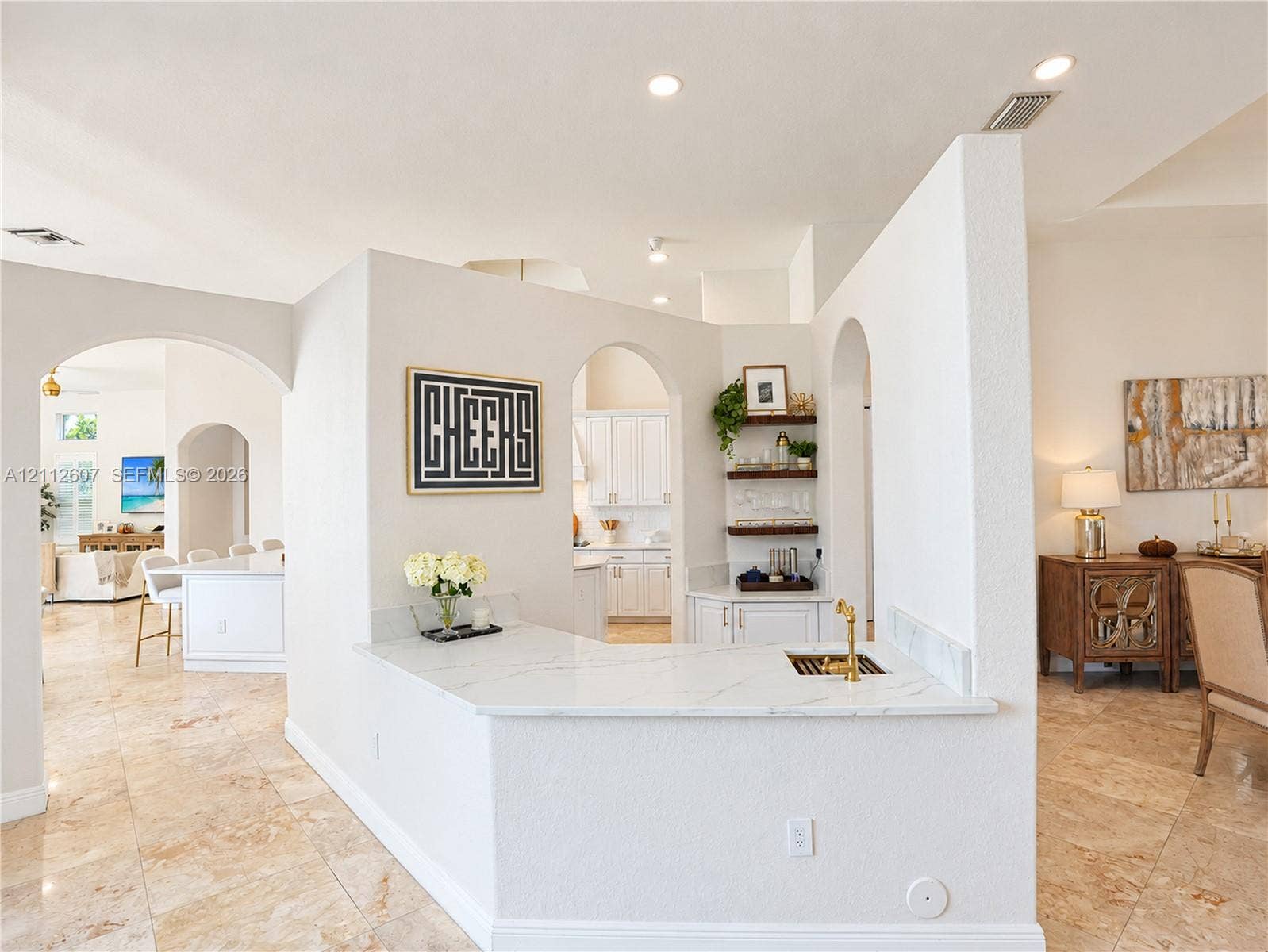 14443 S Jockey Circle S, Davie, FL 33330 Custom wet bar featuring a stone-look countertop, brass-finish faucet, built-in cabinetry, arched entryways, and stone-finish flooring