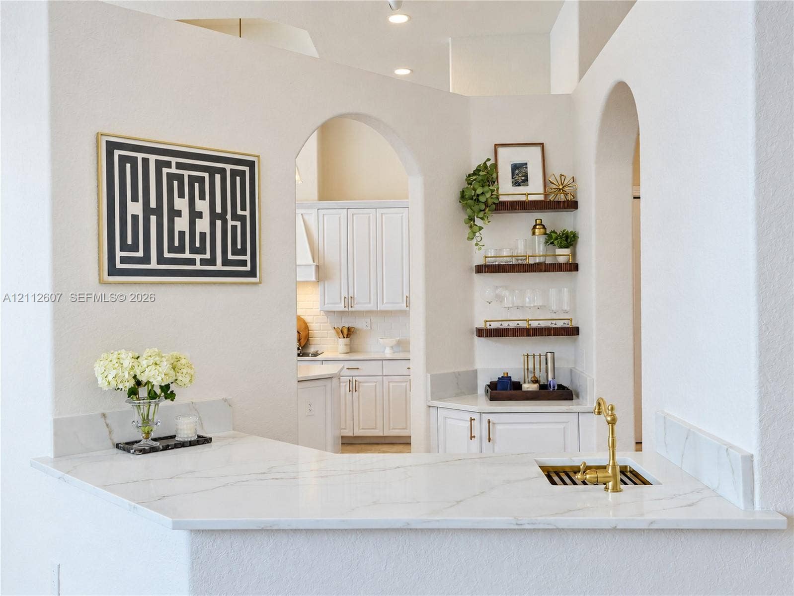 14443 S Jockey Circle S, Davie, FL 33330 Built-in wet bar featuring stone-finish countertop, undermount sink with brass-finish faucet, and custom shelving, framed by architectural archways