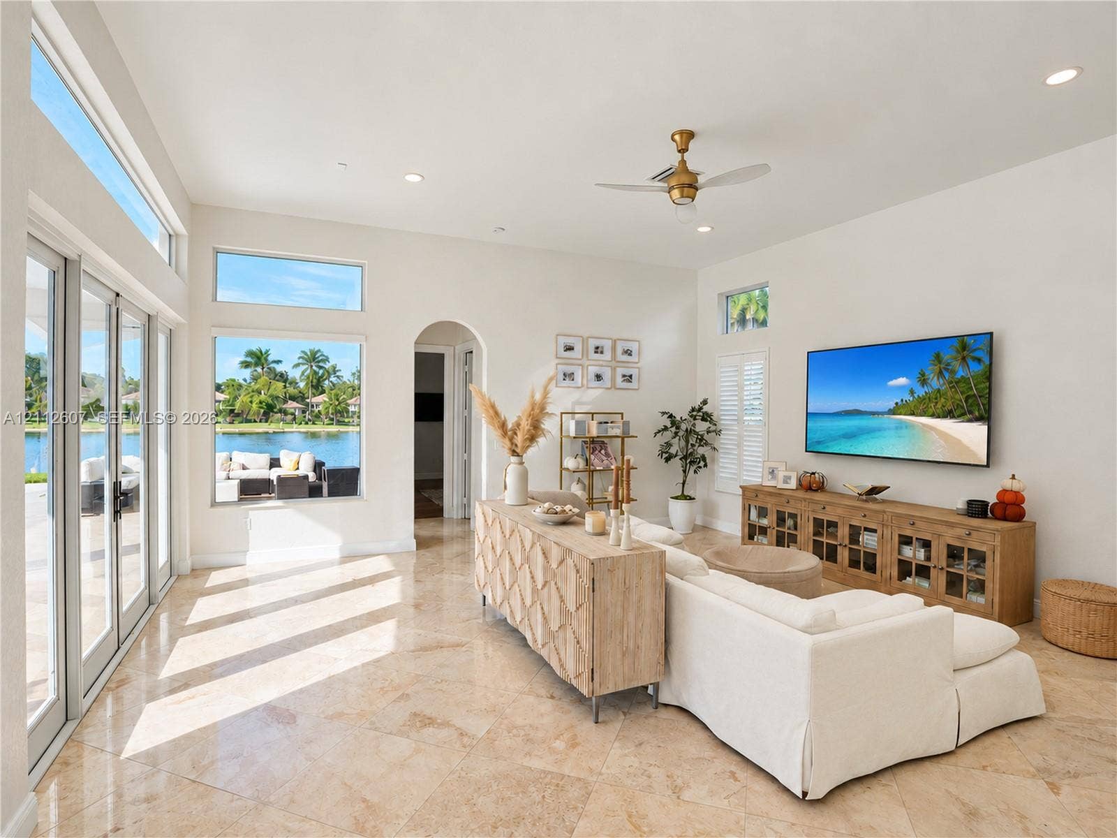 14443 S Jockey Circle S, Davie, FL 33330 Living area featuring expansive windows, natural stone flooring, high ceilings, an arched doorway, and a brushed gold ceiling fan