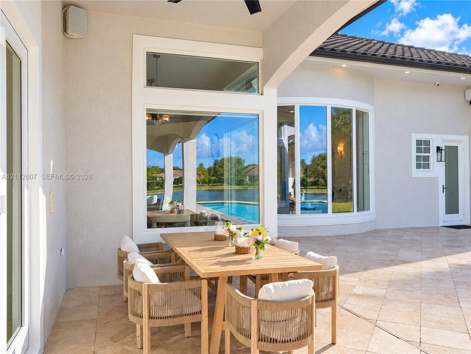 14443 S Jockey Circle S, Davie, FL 33330 Covered lanai featuring neutral stone tile flooring, an integrated ceiling fan, expansive glass picture windows, and a curved architectural wall detail
